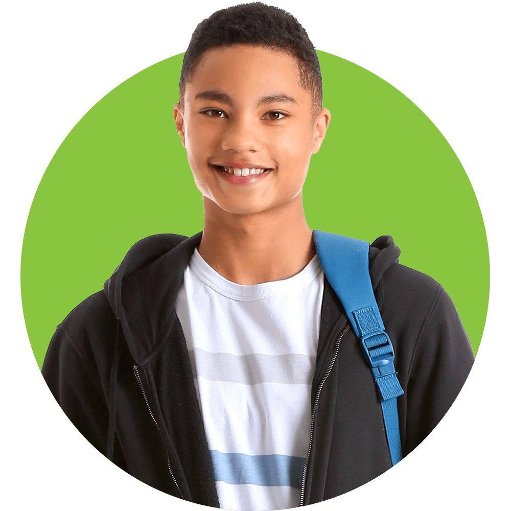 A teen boy stands with a big open mouth smile looking at the camera.