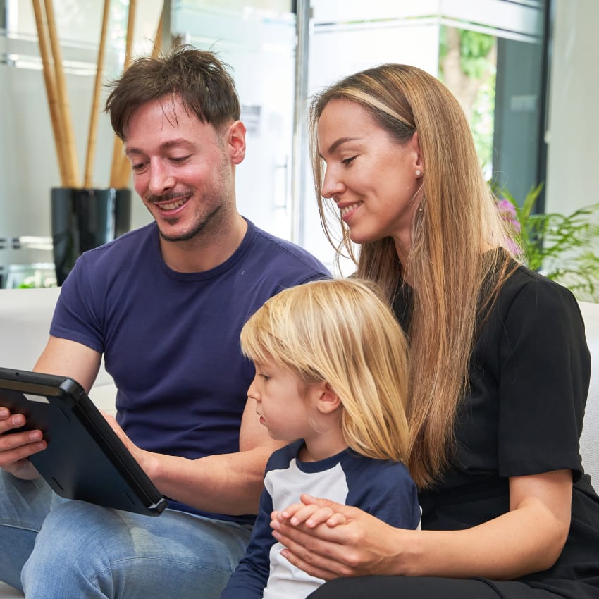 A family sits together in a waiting room while looking ta a tablet.