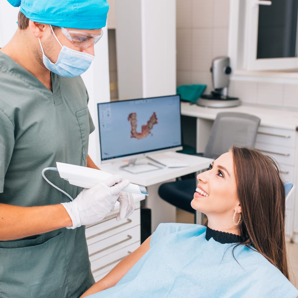 A dental professional holds a digital scanning device while the patient sits in the chair smiling.