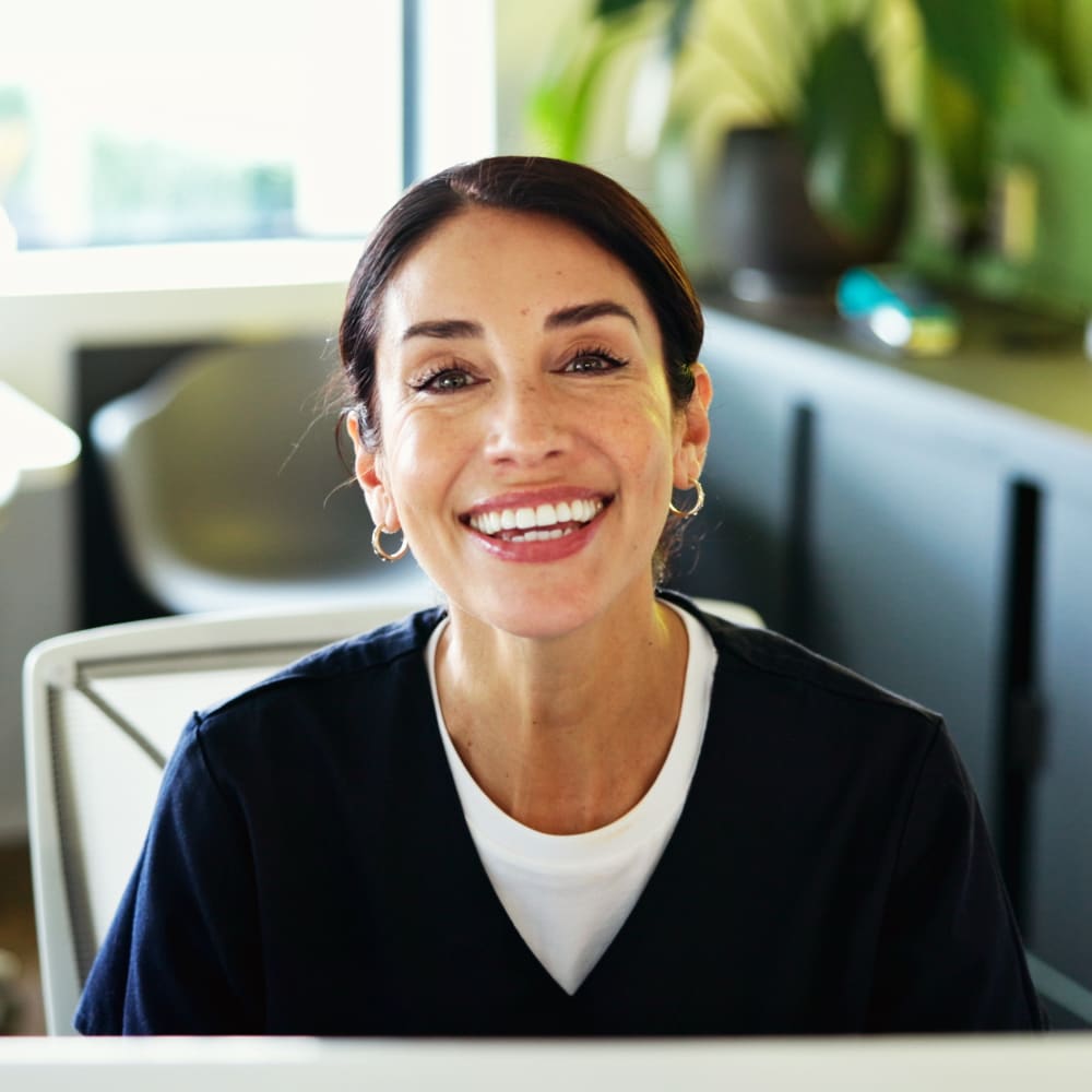 A dental assistant is smiling brightly while sitting at the desk in the office.