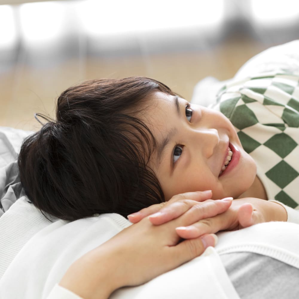 A young boy lays on a bed on a womans lap while smiling and looking up.