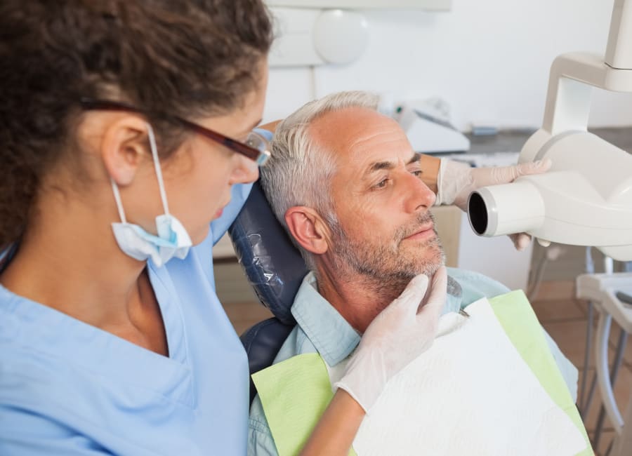 An assistant lines up a digital X-ray machine with the side of a patient's mouth.