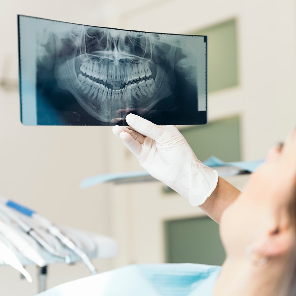 A dental professional holds a panoramic X-ray image up in front of a patient while in the clinic.